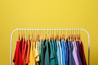 Rack with bright clothes on yellow background. Rainbow colors