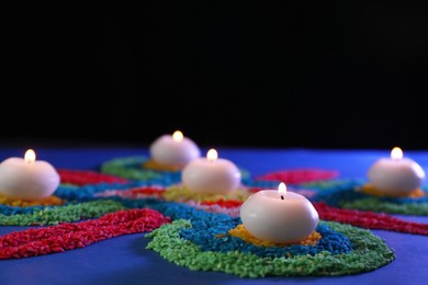 Photo of Diwali celebration. Burning candles and colorful rangoli on table against black background, closeup