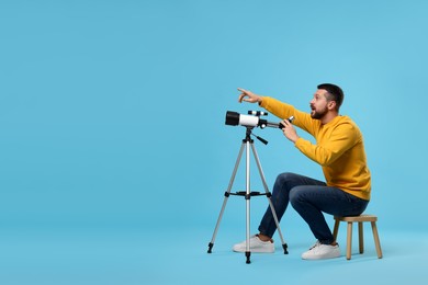 Photo of Excited astronomer with telescope pointing at something on light blue background. Space for text