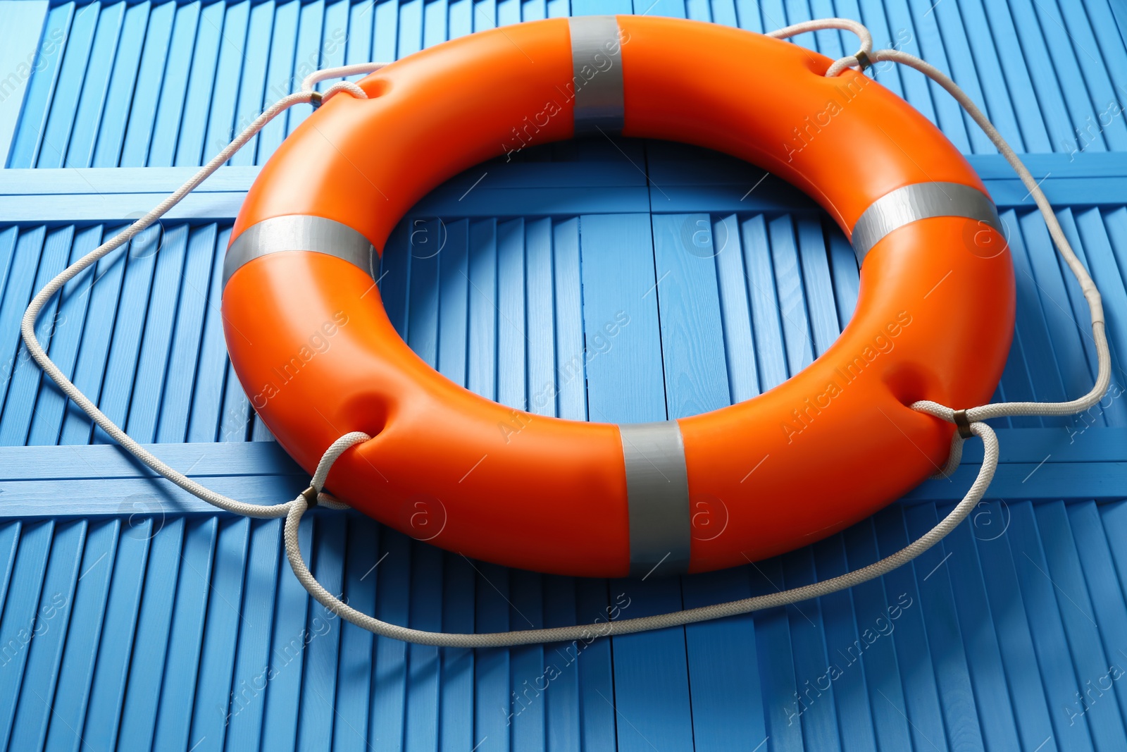 Photo of Orange lifebuoy on blue wooden background, closeup. Rescue equipment