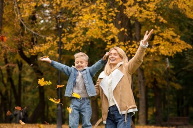 Happy mother and her son playing with dry leaves in autumn park