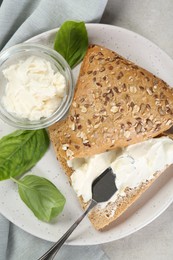 Pieces of bread with cream cheese and basil leaves on light gray table, top view