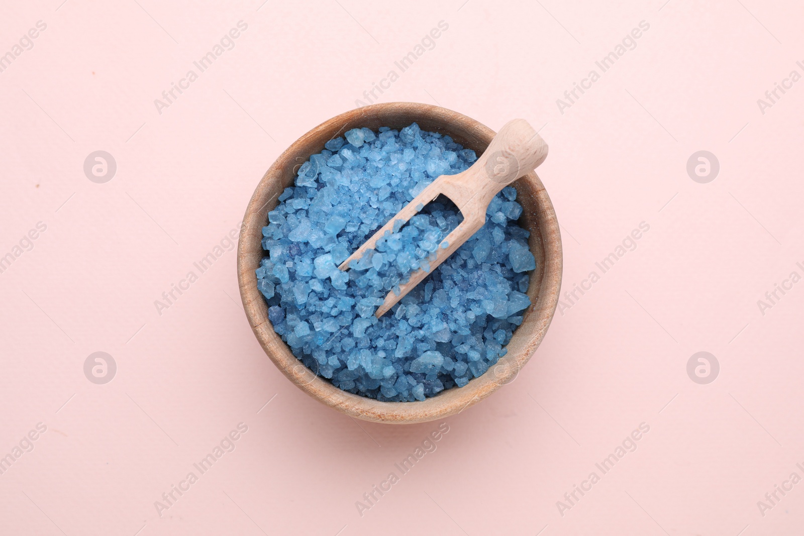 Photo of Bowl and scoop with blue sea salt on pale pink background, top view