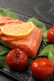 Tasty grilled salmon with tomatoes, spinach and lemon on table, closeup