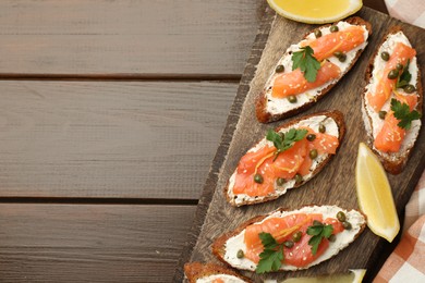 Photo of Tasty canapes with salmon, capers, lemon and cream cheese on wooden table, top view. Space for text