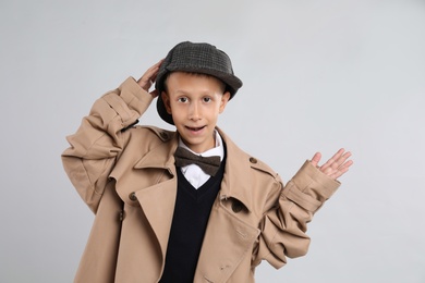 Cute little detective in hat and coat on grey background