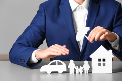 Photo of Male insurance agent covering paper family, car and home with umbrella cutout at table, closeup