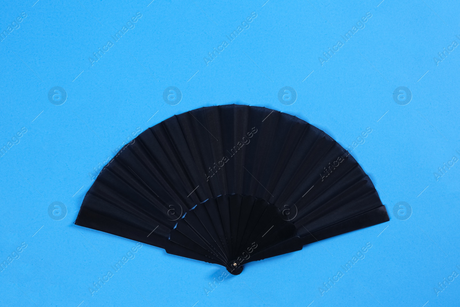 Photo of Black hand fan on light blue background, top view