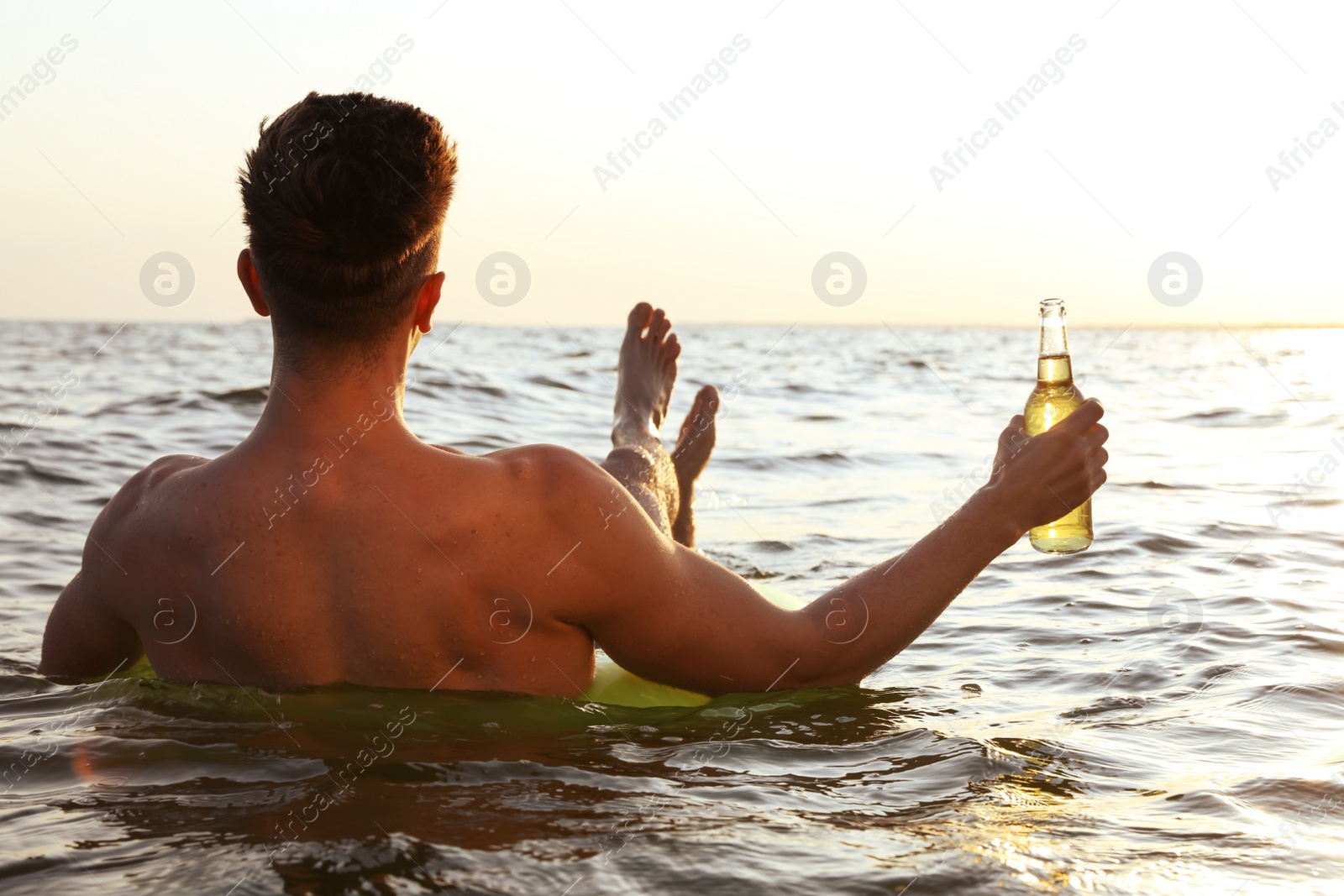 Photo of Young man with drink on inflatable ring in sea, back view