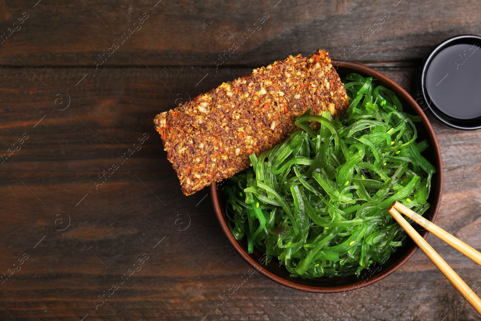 Photo of Tasty seaweed salad in bowl served on wooden table, flat lay. Space for text