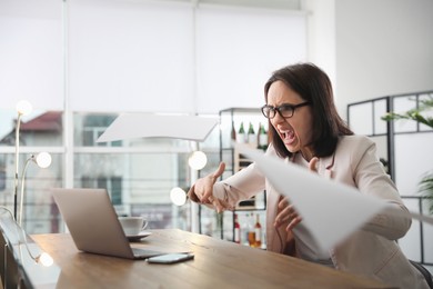 Photo of Emotional businesswoman throwing papers at workplace in office. Online hate concept