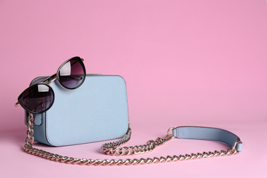 Stylish woman's bag and sunglasses on light pink background