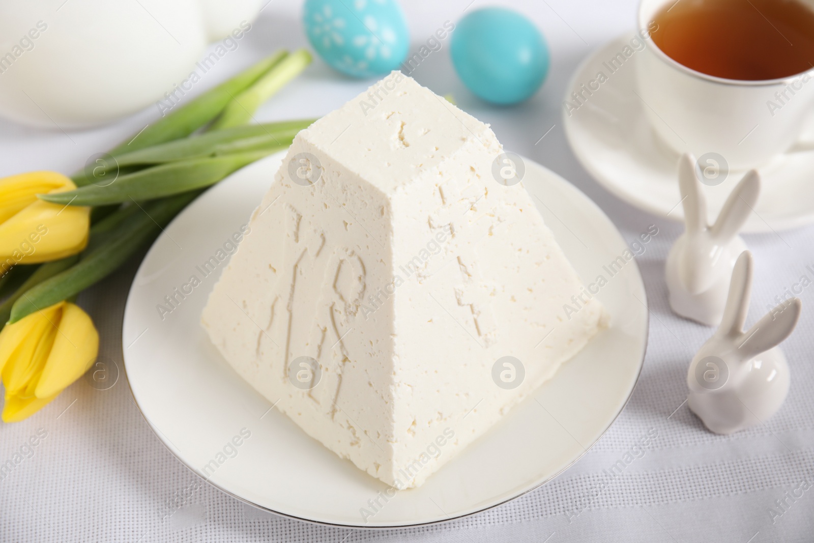 Photo of Traditional cottage cheese Easter paskha, decorative bunnies and yellow tulips on white fabric