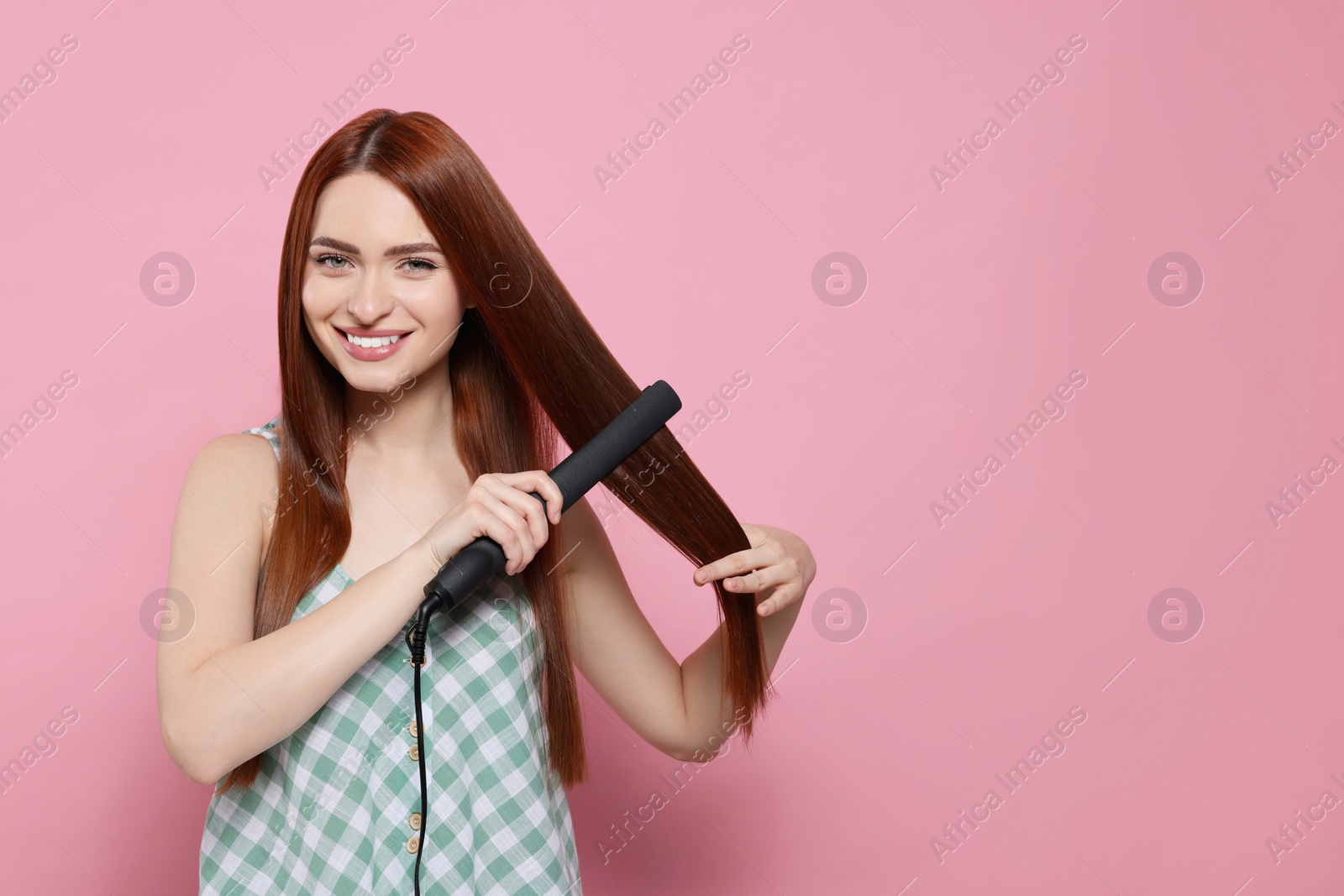 Photo of Beautiful woman using hair iron on pink background, space for text