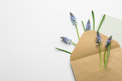 Envelope with beautiful spring muscari flowers and card on light background, flat lay. Space for text