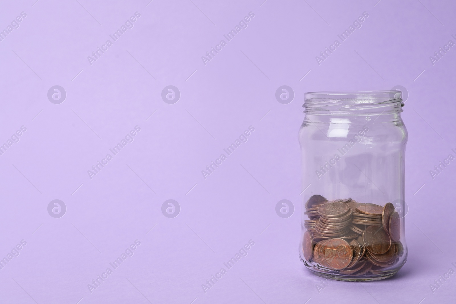 Photo of Glass jar with coins on lilac background, space for text