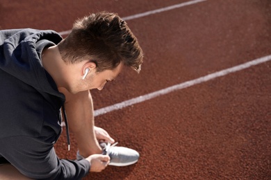 Photo of Young sportsman with wireless earphones at stadium