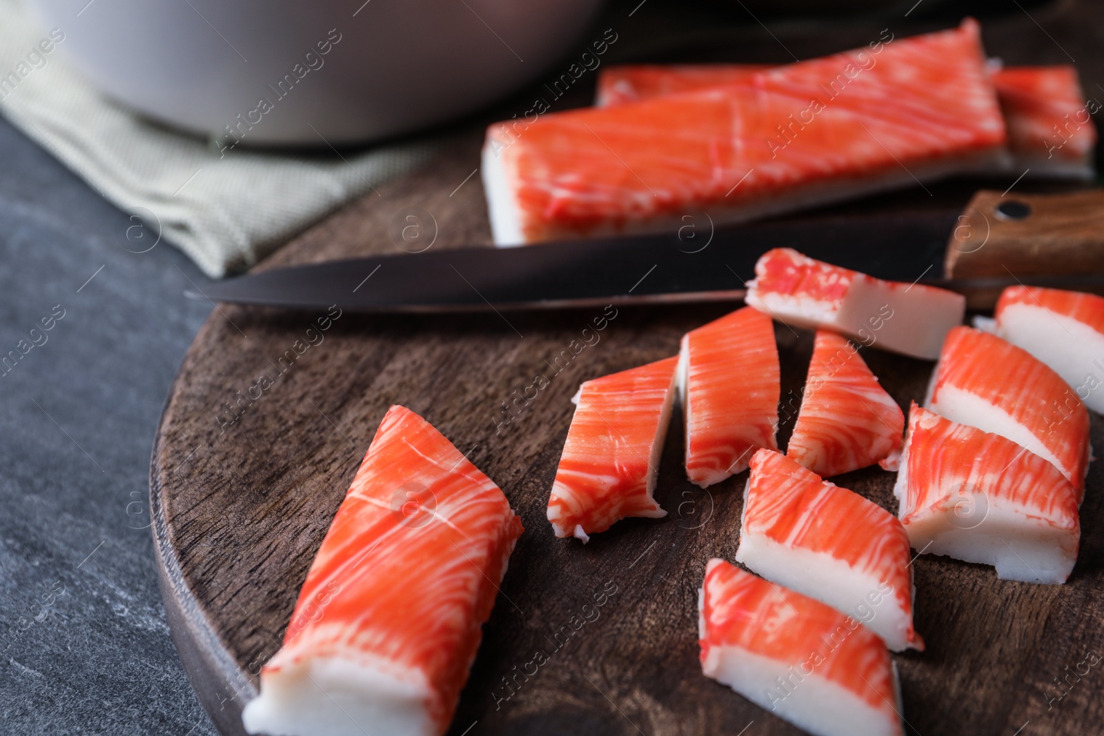 Photo of Sliced crab sticks and knife on wooden cutting board, closeup