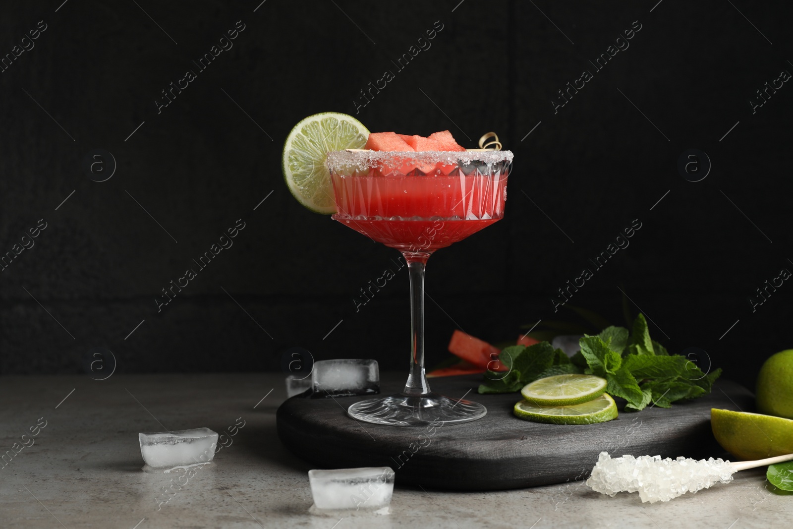 Photo of Cocktail glass of delicious fresh watermelon juice, lime, mint and ice on grey table