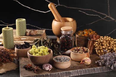 Photo of Many different dry herbs, mortar with pestle and candles on dark grey table