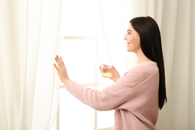 Photo of Beautiful young woman with tasty lemon water near window