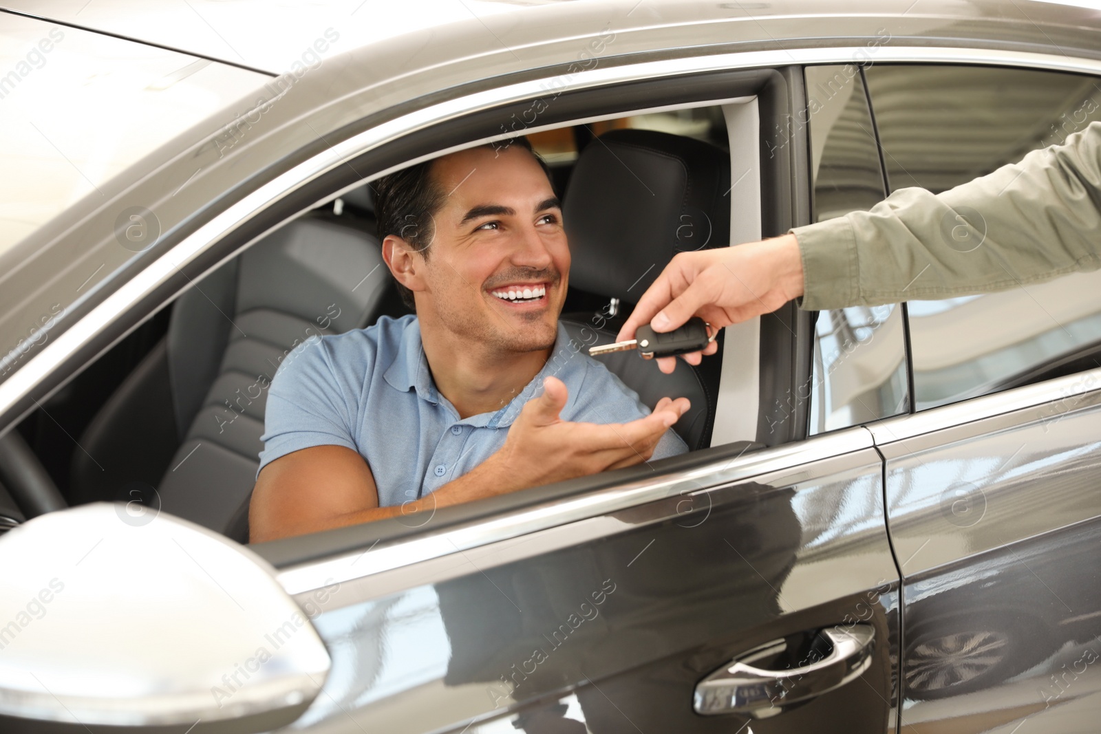 Photo of Young salesman giving car key to customer in modern auto dealership, closeup