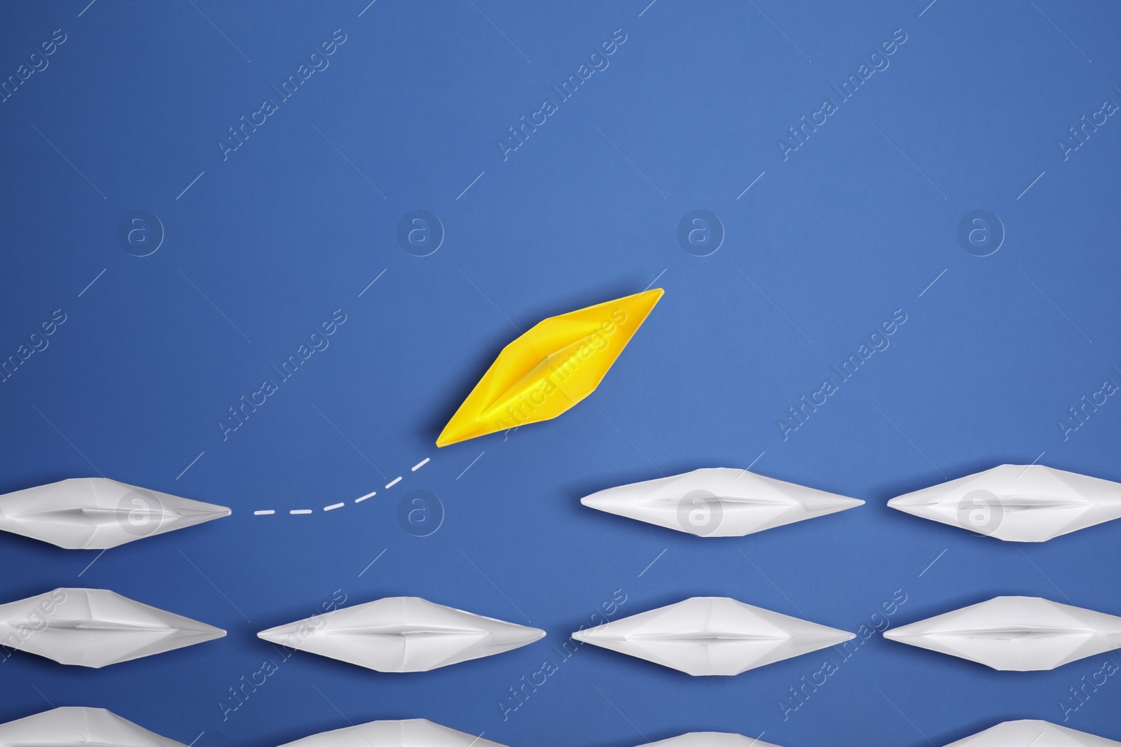 Photo of Yellow paper boat floating away from others on blue background, flat lay with space for text. Uniqueness concept