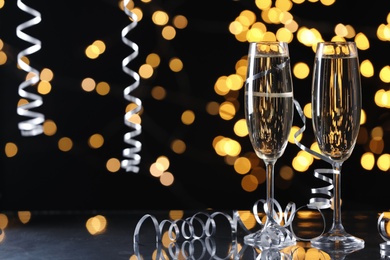 Photo of Glasses of champagne and serpentine streamers against black background with blurred lights. Space for text