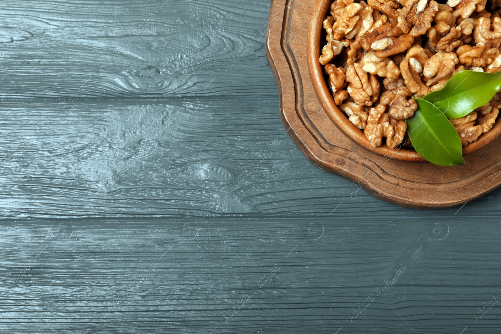 Photo of Dish with walnuts on wooden background, top view. Space for text