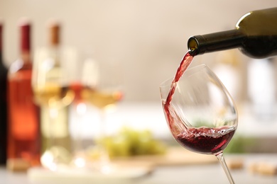 Photo of Pouring red wine from bottle into glass on blurred background. Space for text