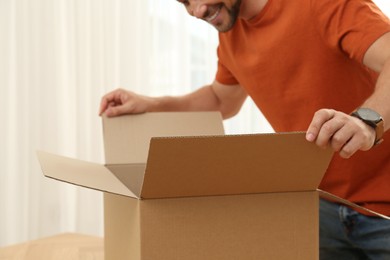 Photo of Happy man opening parcel indoors, closeup. Internet shopping