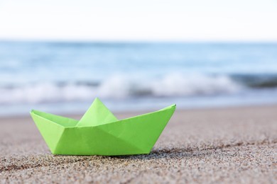 Photo of Light green paper boat near sea on sandy beach, space for text