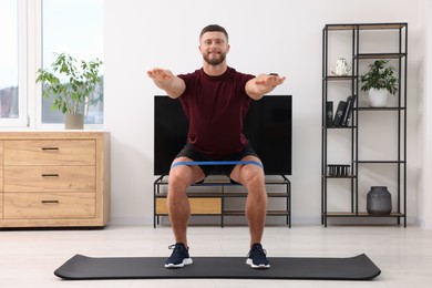Athletic man doing exercise with elastic resistance band on mat at home