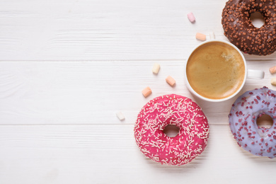 Flat lay composition with yummy donuts on white wooden background, space for text