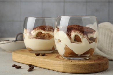 Photo of Delicious tiramisu in glasses and scattered coffee beans on light table