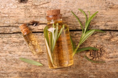 Aromatic essential oils in bottles and rosemary on wooden table, flat lay