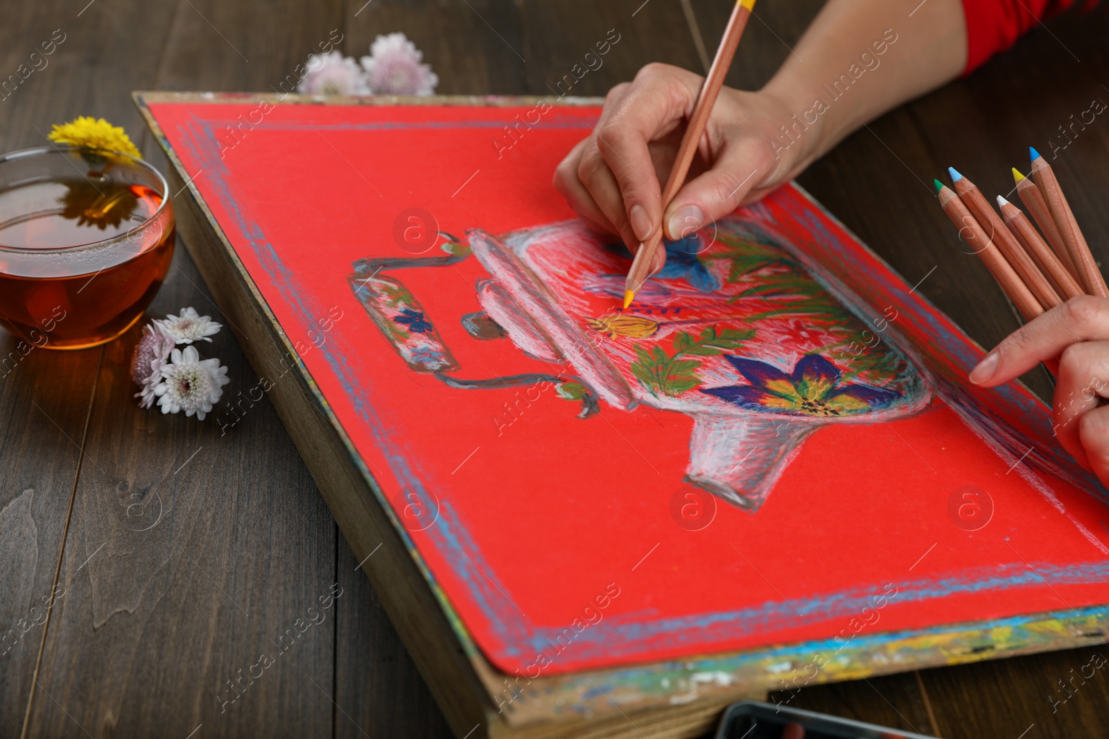 Photo of Woman drawing beautiful kettle with pastel pencil at wooden table, closeup