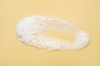 Photo of Spot of white washing foam on yellow background, top view