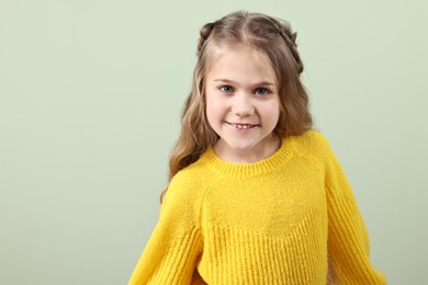 Photo of Cute little girl with braided hair on light green background. Space for text