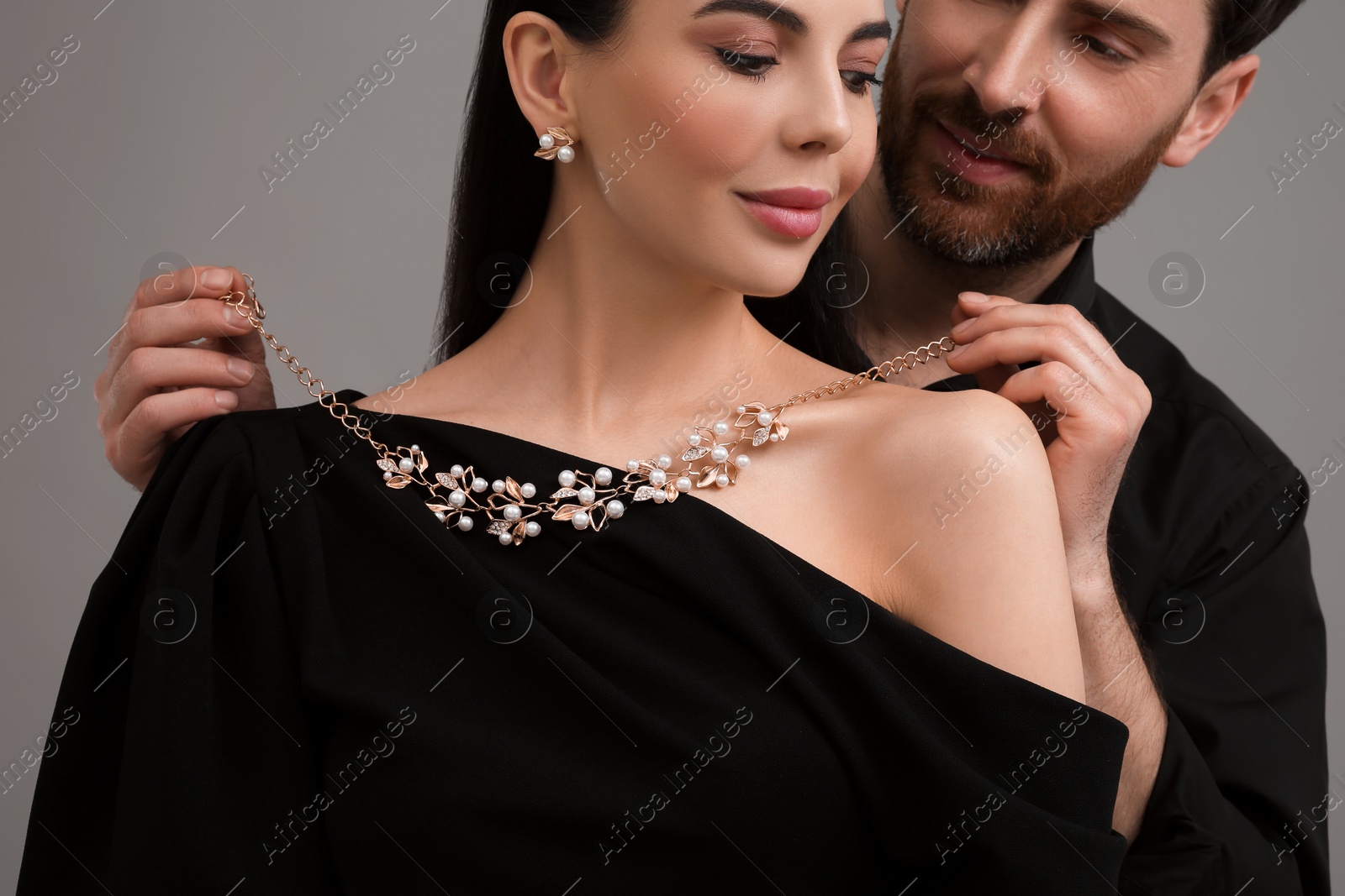 Photo of Man putting elegant necklace on beautiful woman against grey background, closeup