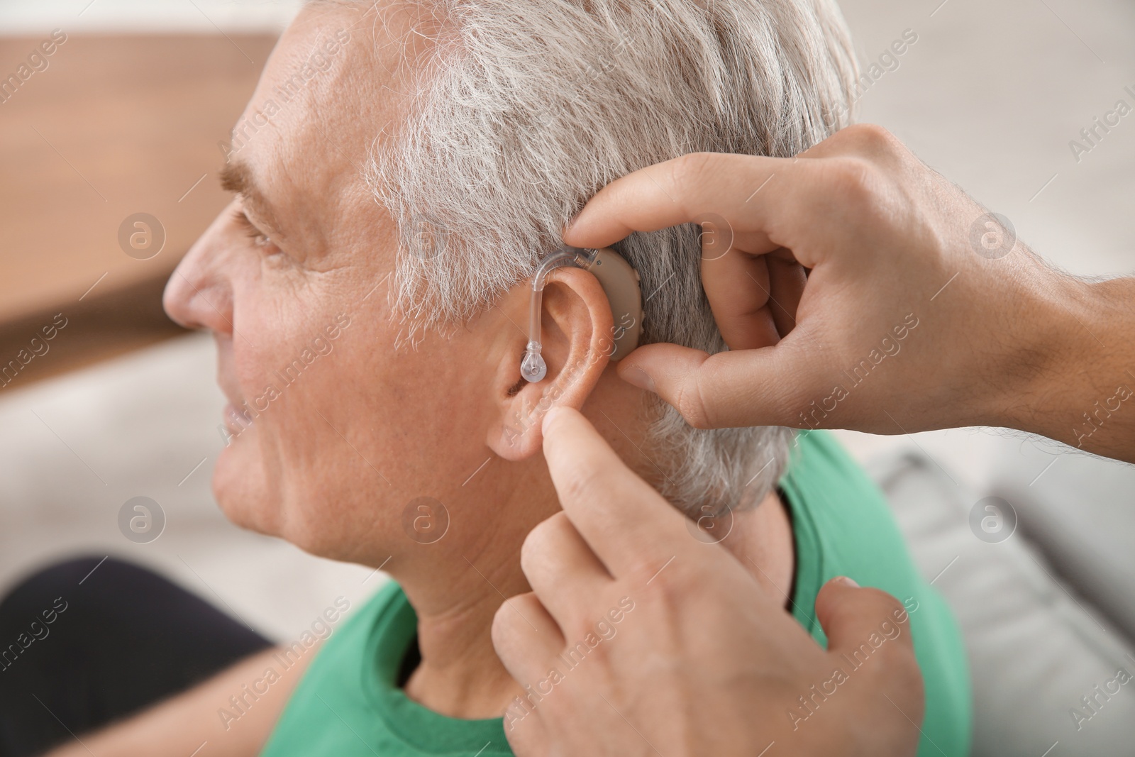Photo of Young man putting hearing aid in father's ear indoors, closeup