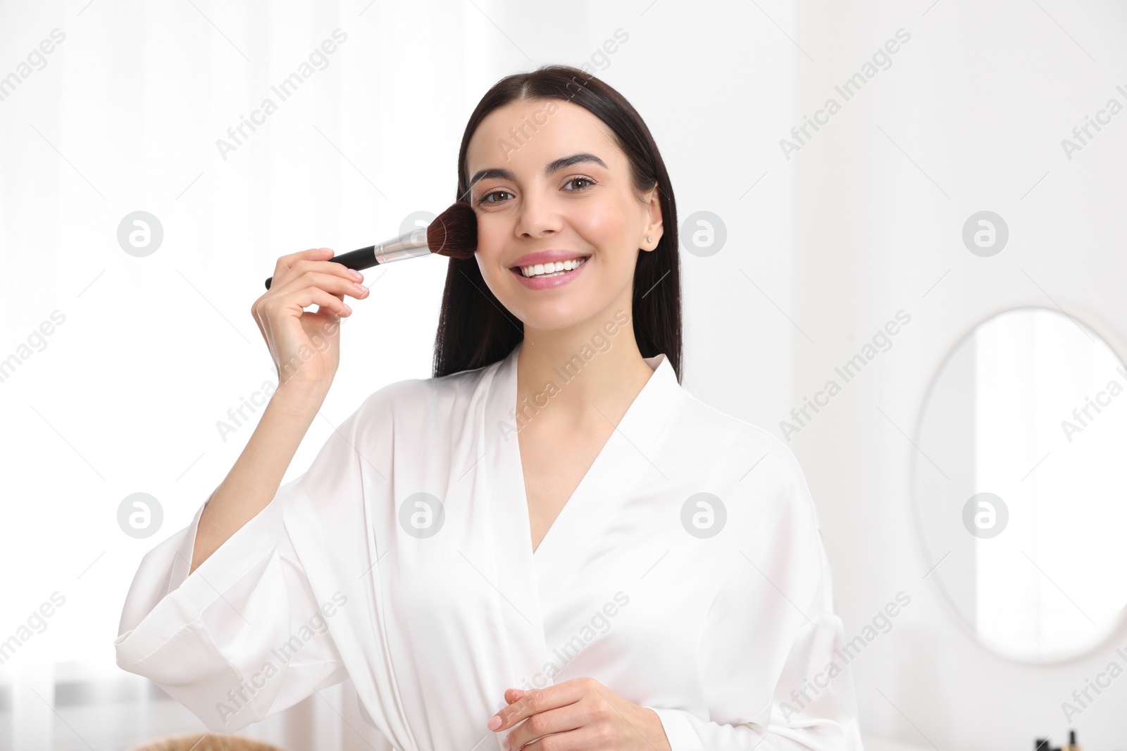 Photo of Beautiful young woman applying makeup with brush at home