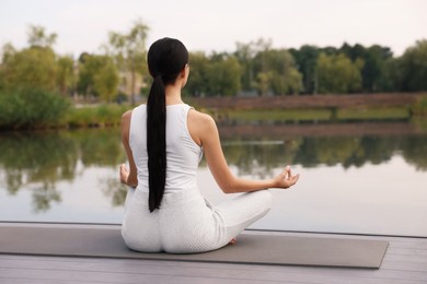 Woman practicing Padmasana on yoga mat outdoors, back view. Lotus pose