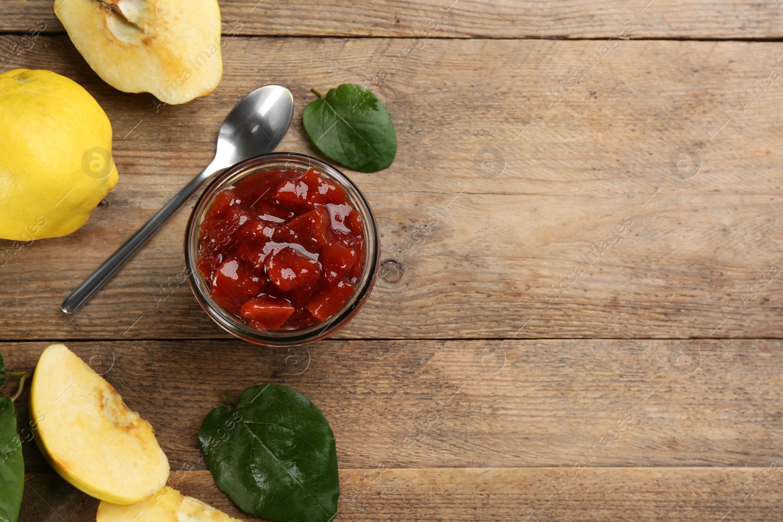 Photo of Delicious quince jam, fruits, leaves and spoon on wooden table, flat lay. Space for text