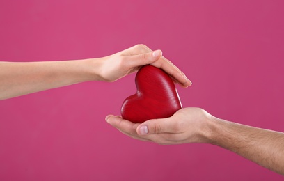 Man and woman holding decorative heart on color background, closeup