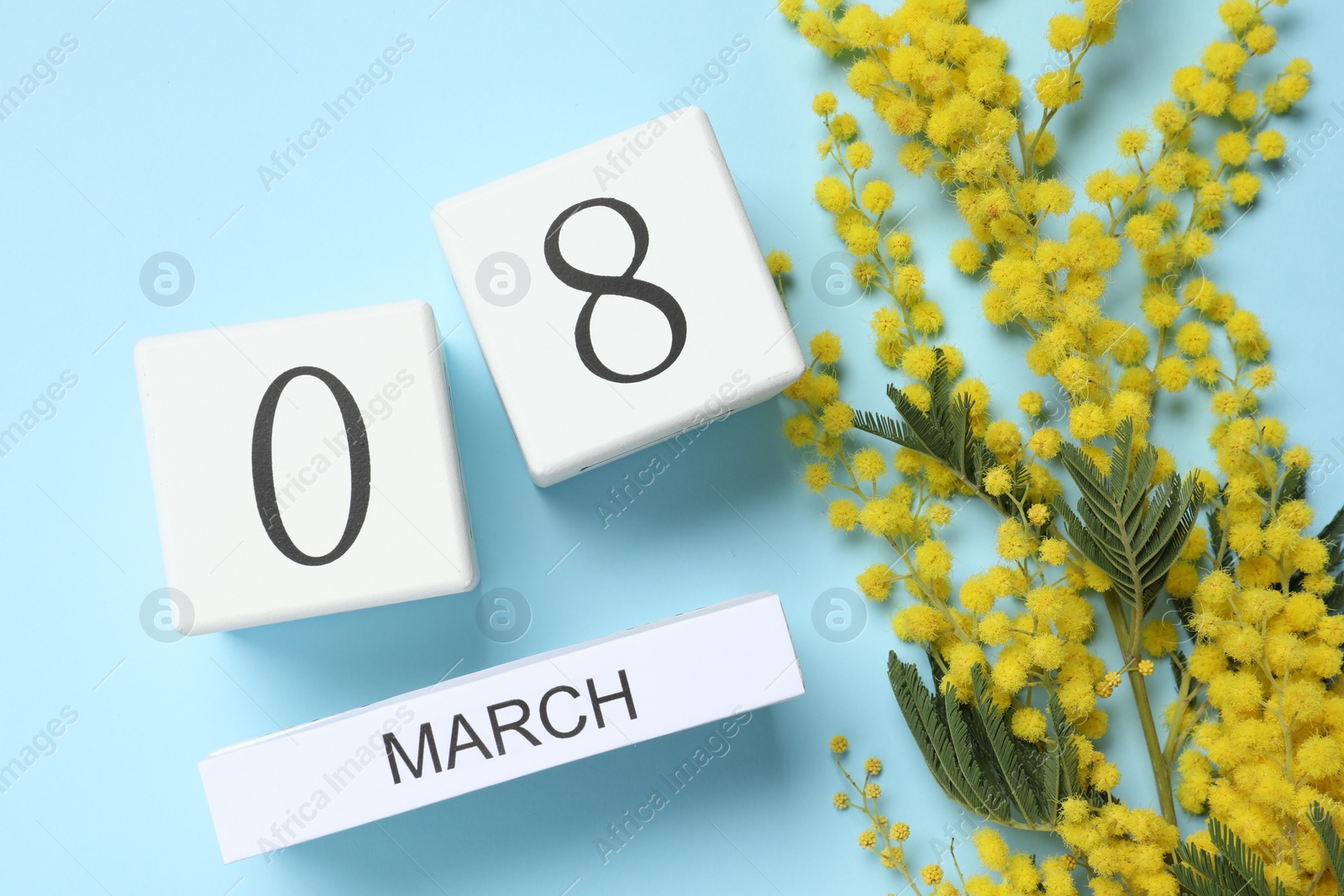 Photo of March 8 - International Women's Day. Greeting card design with beautiful yellow mimosa flowers and wooden block calendar on light blue background, flat lay