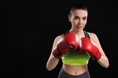Portrait of beautiful woman in boxing gloves on black background. Space for text