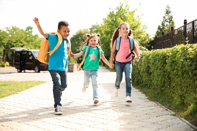 Photo of Cute little children with backpacks running outdoors. Elementary school