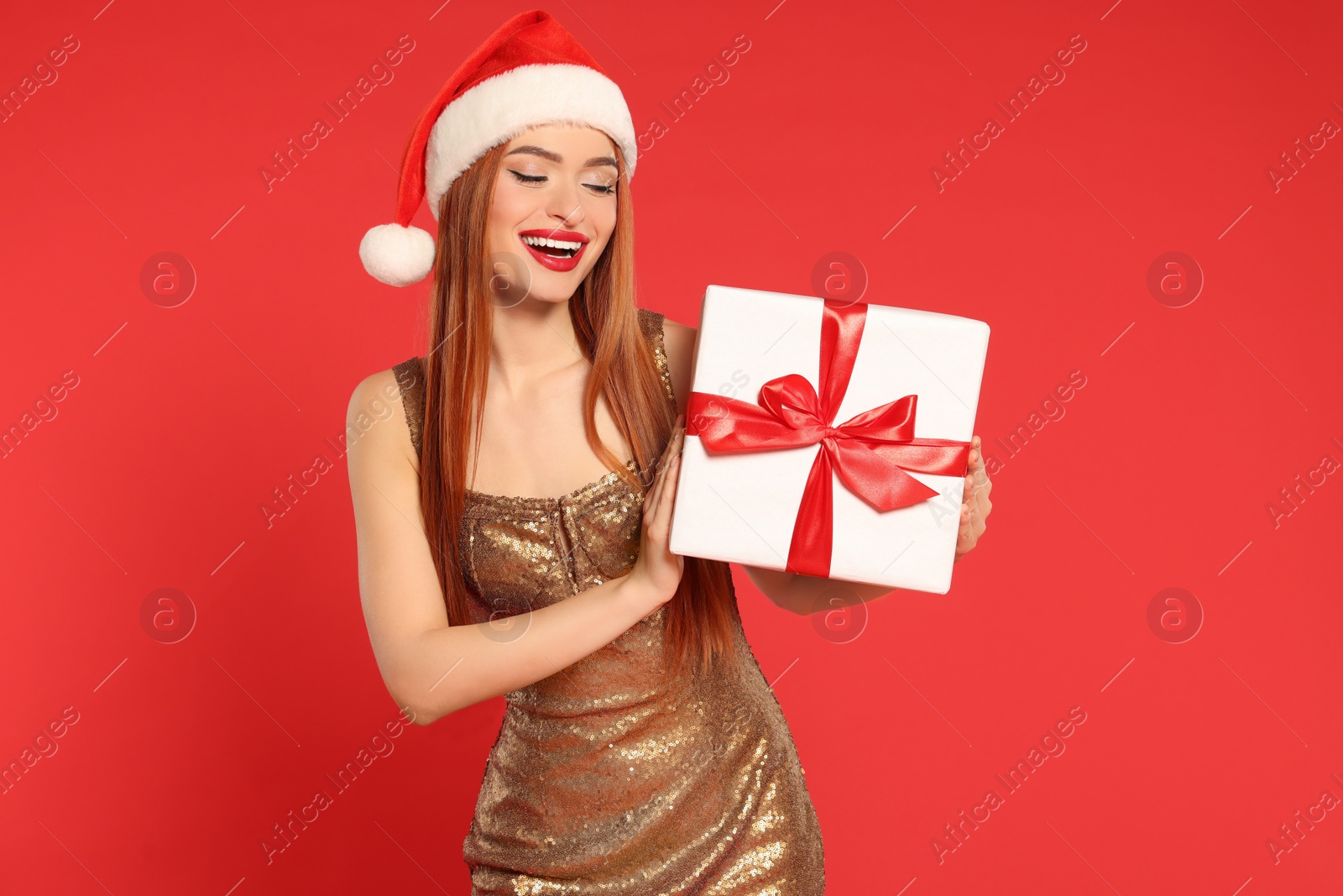 Photo of Young woman in Santa hat with Christmas gift on red background