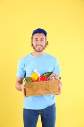 Photo of Delivery man holding wooden crate with food products on color background
